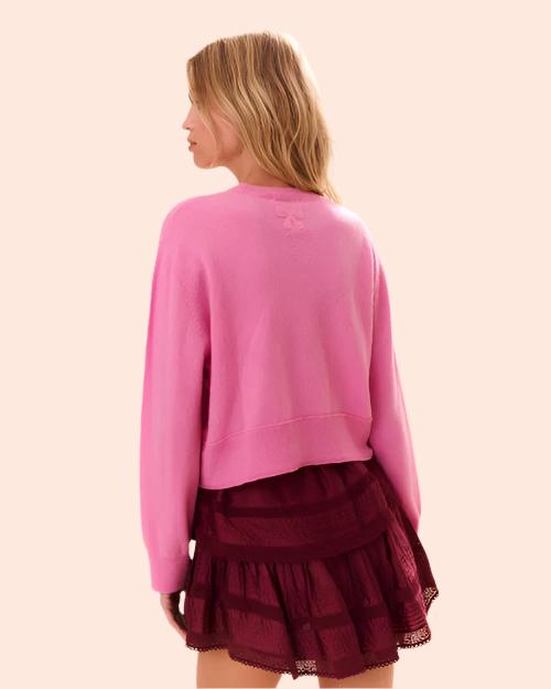 Back view of a person is wearing a bright pink sweater with long sleeves. The sweater is paired with a tiered, ruffled skirt in a darker shade of maroon. On the top part of the back of the sweater, there s an embroider bow.