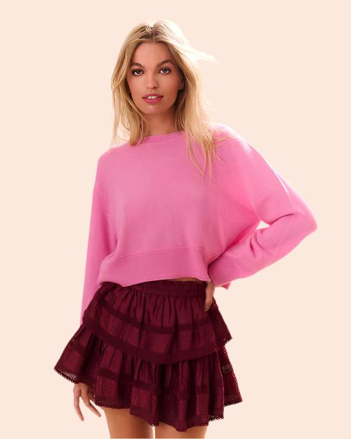 A person is wearing a bright pink sweater with long sleeves. The sweater is paired with a tiered, ruffled skirt in a darker shade of maroon.