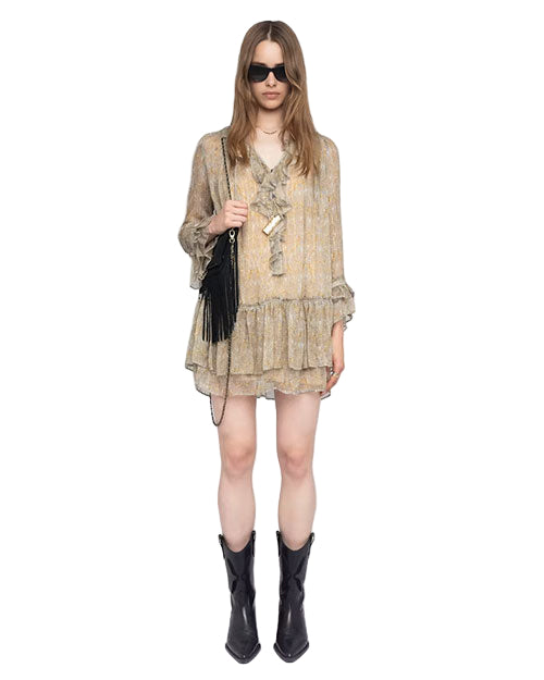 Person wearing a light-colored, patterned dress with ruffles, long sleeves, and a layered skirt, paired with black cowboy boots and a black fringed handbag over the left shoulder. 