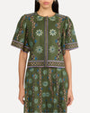A zoomed in frontal view of a person standing and wearing a matching green outfit with intricate patterns. The outfit consists of short-sleeved top and matching shorts, both adorned with floral and geometric designs in white, blue, and purple colors. The background is plain white.