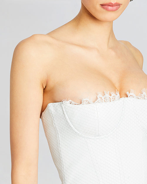 A close-up of a cracked leather strapless white mini dress with a straight neckline. The dress features lace trim at the bust. 