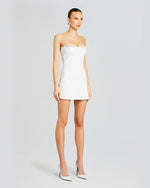 A model wearing a strapless white mini dress with a straight neckline and a fitted silhouette. The dress features lace trim at the bust and hemline. The model is styled with white high heels.