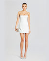 A model wearing a strapless white mini dress with a straight neckline and a fitted silhouette. The dress features lace trim at the bust and hemline. The model is styled with a small metallic clutch and white high heel.