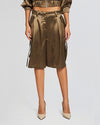 A close up of a pair of high-waisted, olive green satin shorts with a tie-up belt and large pockets on each side. The shorts have a wide leg design and reach just above the knee. They are paired with beige high-heeled shoes and a matching satin jacket.