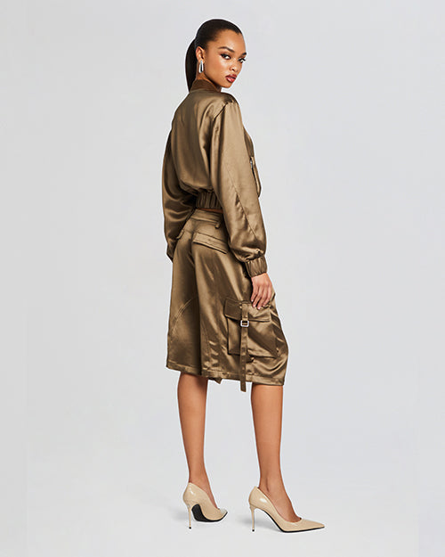 A back view of A pair of high-waisted, olive green satin shorts with a tie-up belt and large pockets on each side. The shorts have a wide leg design and reach just above the knee. They are paired with beige high-heeled shoes and a matching satin jacket.