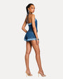Back view a woman wearing a denim top and matching shorts, accessorized with silver earrings on a white background