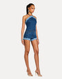 Side view of a woman wearing a blue denim shorts and halter top with nude heels on a white background