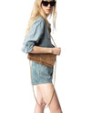A person wearing black sunglasses, a denim shirt and denim shorts, holding a brown leather handbag with a chain strap.