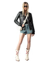 A person wearing a black leather jacket, denim shorts, and white cowboy boots with red designs, carrying a small white crossbody bag.