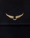 A close-up view of a black fabric flap with stitching at the bottom, and a detailing gold wing detail adorned in the center.