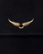 A close-up view of a black fabric flap with stitching at the bottom, and a detailing gold wing detail adorned in the center.