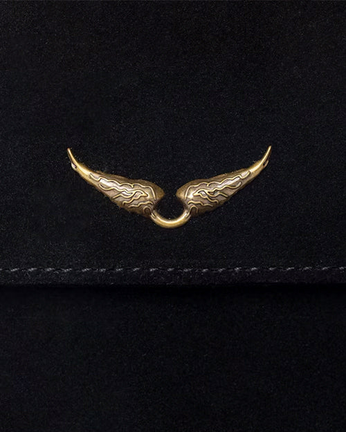 A close-up view of a black fabric flap with stitching at the bottom, and a detailing gold wing detail adorned in the center.