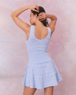 A back view of a light blue dress with a fitted bodice and flared skirt, featuring delicate ruffle details, a zigzag lace pattern, and vertical ribbing.