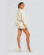 Back view of a model wearing a beige satin romper with a collared jacket top and shorts. The back of the romper has two pockets with flaps and cinching on the sleeves.