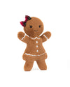 Plush toy shaped like a gingerbread person, featuring brown fabric, white icing-like trim on the arms, neck, and hem of its dress, three white buttons down the front, a red plaid bow on its head, black eyes, and a stitched smile.