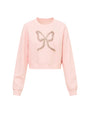 Light pink cropped sweatshirt with long sleeves, featuring a decorative bow design made of small, shiny embellishments on the front center.