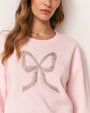 Person wearing a light pink sweatshirt with an embellished bow design on the front.
