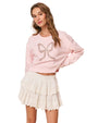Person wearing a light pink sweatshirt with a decorative bow design on the front, paired with a white tiered lace skirt.