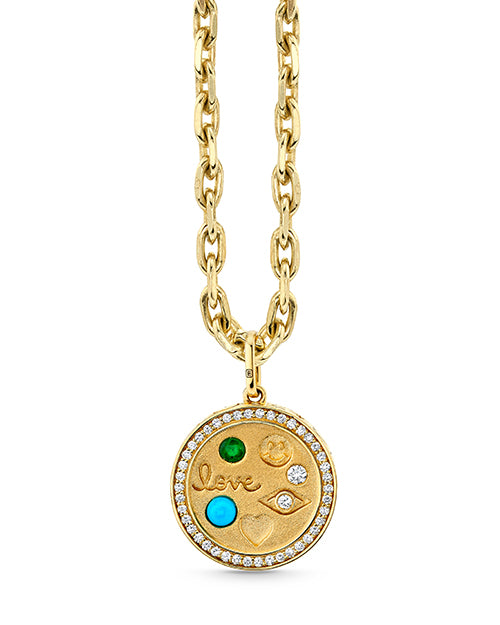 A gold necklace featuring a circular pendant with the word ‘love’ embossed in the center, surrounded by small gemstones and diamonds. The chain is made of thick, interlocking gold links.