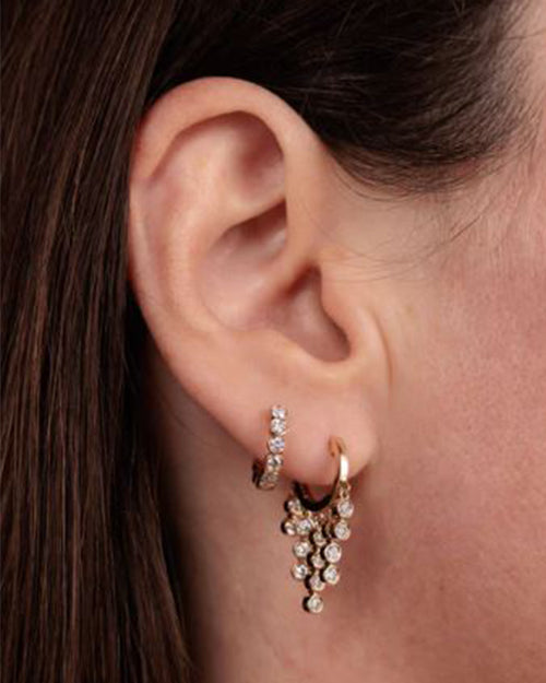 Close up on model's ear wearing round bezel earing  layered with  a second earring to match.