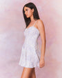 A model in a short white dress with a subtle blue floral pattern. The dress features thin straps, a fitted bodice with a sweetheart neckline, and flares out into an A-line skirt.