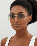 Model wearing aviator-style sunglasses with a thin gold frame and clear violet lenses.  