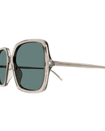 Side view of oversized square-framed sunglasses with a thin silver tone metallic frame and green lenses. Temples feature 'SAINT LAURENT' lettering in silver. 