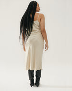 Back view, model wearing dress with black boots on a nude color background.