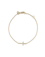 A delicate gold chain bracelet with a small, sideways-set cross pendant adorned with white diamonds. The bracelet has an adjustable clasp and is displayed against a plain, light background.