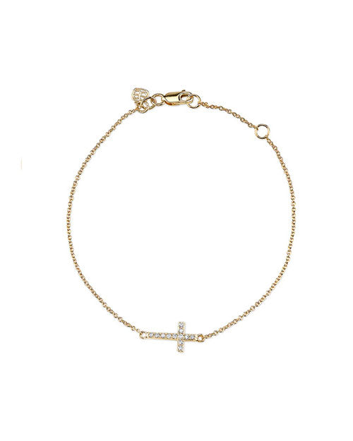 A delicate gold chain bracelet with a small, sideways-set cross pendant adorned with white diamonds. The bracelet has an adjustable clasp and is displayed against a plain, light background.