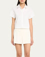 A person wearing a white, short-sleeved, button-up shirt with a collar and white shorts. The shirt and shorts have simple and clean designs with no visible patterns or logos. The persons face is not visible.