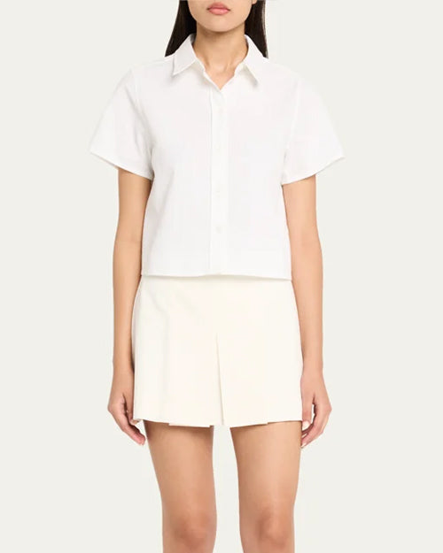 A person wearing a white, short-sleeved, button-up shirt with a collar and white shorts. The shirt and shorts have simple and clean designs with no visible patterns or logos. The persons face is not visible.