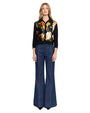 Person standing and facing forward, wearing a black long-sleeve shirt with a vibrant floral print in yellow, white, and orange. Paired with high-waisted, wide-leg denim jeans featuring prominent vertical seams.