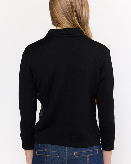 A person with long hair is shown from the back, wearing a black long-sleeve top with a collar and slightly cropped sleeves, paired with blue jeans featuring visible stitching on the back pockets. The background is plain white.