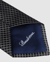 A back view of a necktie with a black and gray geometric pattern. The interior features blue fabric and white lettering.