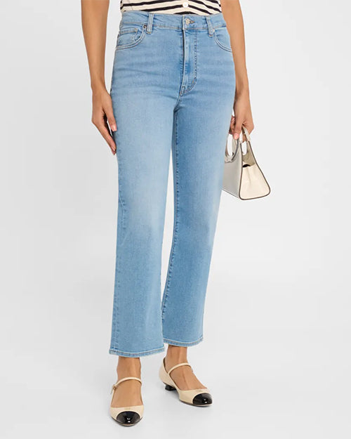 A person wearing light blue high-waisted jeans, a black and white striped top tucked in, and beige shoes with black toe caps. The pants have button and zipper closure and belt loops, as well as two front pockets with a coin pouch. The person is holding a small beige handbag.