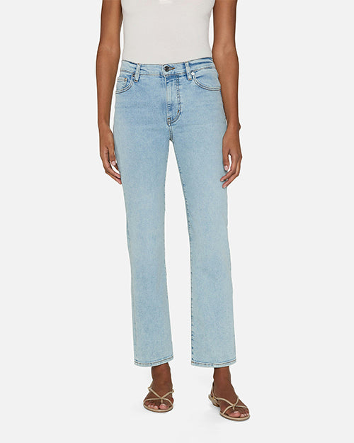 A person wearing light blue jeans and a white sleeveless top tucked in. The jeans are high-waisted with front pockets and straight legs. The pants have button and zipper closure. The person is also wearing open-toe sandals.