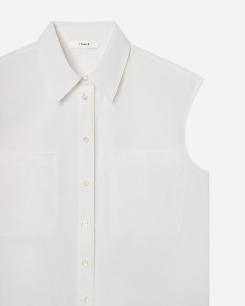 The close-up view of a sleeveless white button-up shirt with a collar. The shirt has small off-white buttons running down the center and two chest pockets. On the inside neckline is a tag which reads "FRAME".