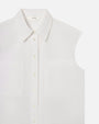 The close-up view of a sleeveless white button-up shirt with a collar. The shirt has small off-white buttons running down the center and two chest pockets. On the inside neckline is a tag which reads "FRAME".