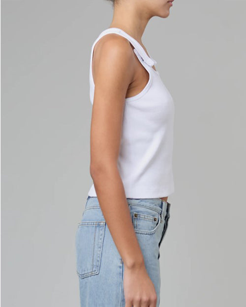 A side view of a model wearing a white tank top with button snap straps that close at the upper chest. The model pairs the shirt with light blue jeans.