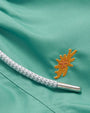 A close-up of embroidered multicolored sea flowers in various poses scattered across the fabric of childrens swim shorts. The shorts have a white drawstring with the brand engraved in the metallic piece.