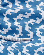 A close-up of swim shorts with a repeating pattern of white silhouettes. There is a white drawstring with a metal aglet at its end.