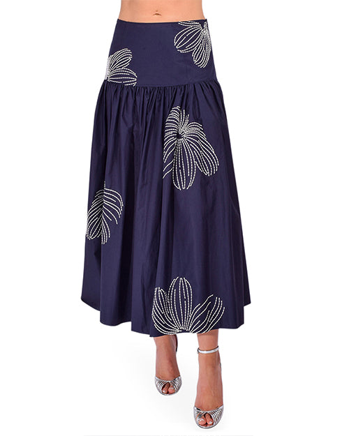 Bottom part of a person wearing a navy blue skirt with white floral patterns and silver heels on a white background 