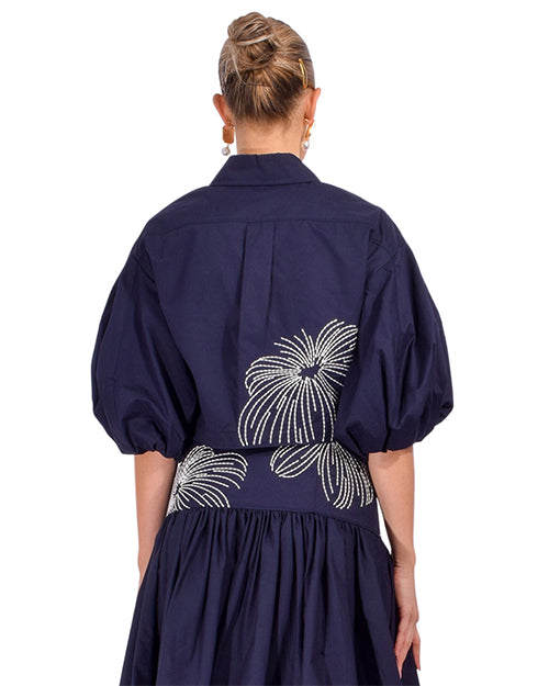 The top back view a person wearing a two piece navy outfit with white floral pattern on a white background