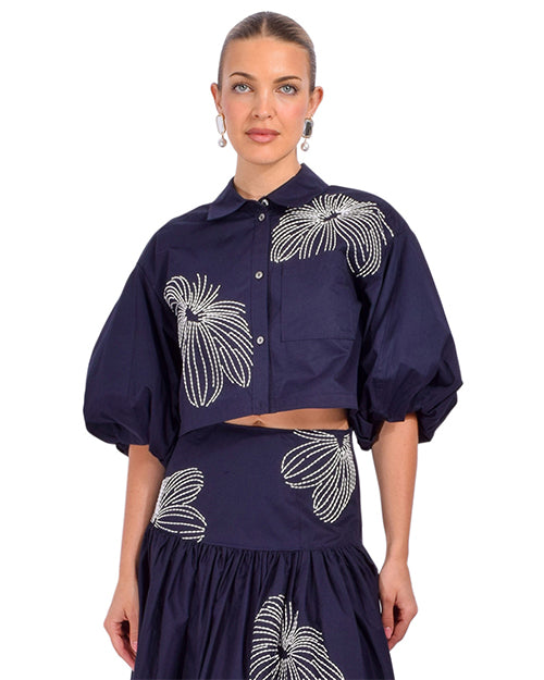 Woman wearing a navy blue two piece outfit with white floral patterns on a white background