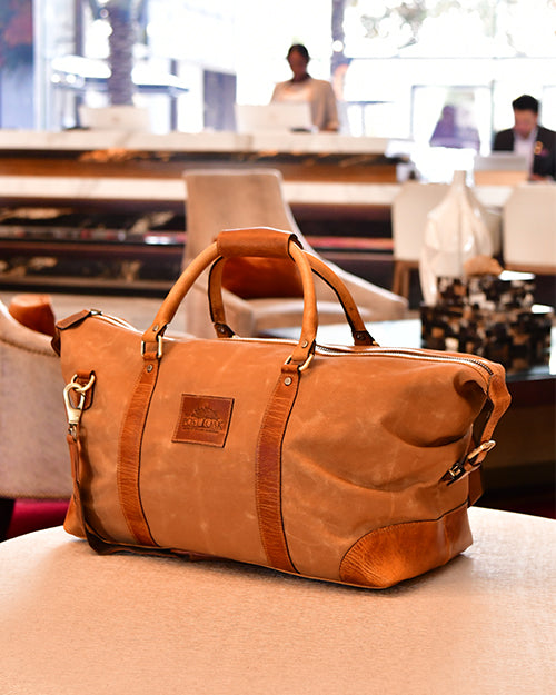 Brown leather duffel bag on a table with a blurred indoor setting in the background