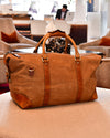 Back view of a brown leather duffel bag on a table in a modern interior setting