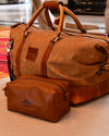 Brown leather duffel bag and toiletry bag with visible brand logo on a solid surface.