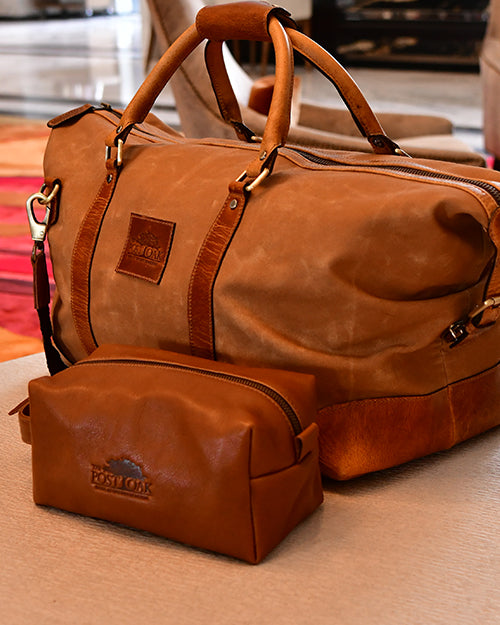 Brown leather duffel bag and toiletry bag with visible brand logo on a solid surface.
