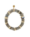 Bracelet made of cylindrical labradorite beads in grayish-green tones with iridescent flashes, accented by gold spacers encrusted with small white gemstones. A round gold charm with an intricate design is positioned at the top.